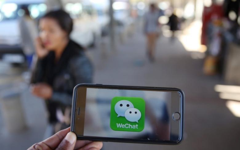 A WeChat logo is displayed on a mobile phone as a woman walks past as she talks on her mobile phone at a taxi rank in this picture illustration taken July 21, 2016. REUTERS/Siphiwe Sibeko/Illustration